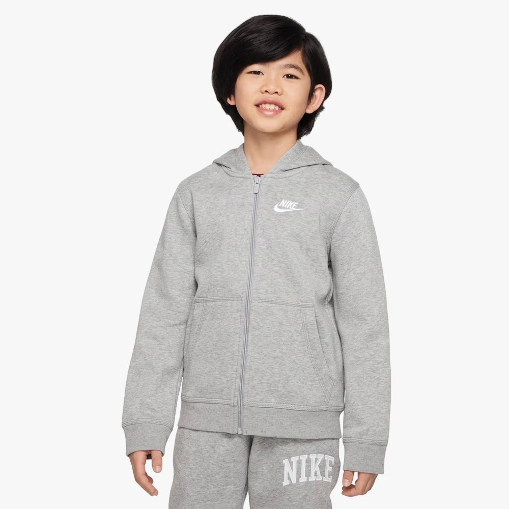 Young boy smiling, wearing a full-zip grey Nike Kids Fz Hoody and matching grey Nike sweatpants, standing in a studio.
