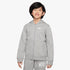 Young boy smiling, wearing a full-zip grey Nike Kids Fz Hoody and matching grey Nike sweatpants, standing in a studio.