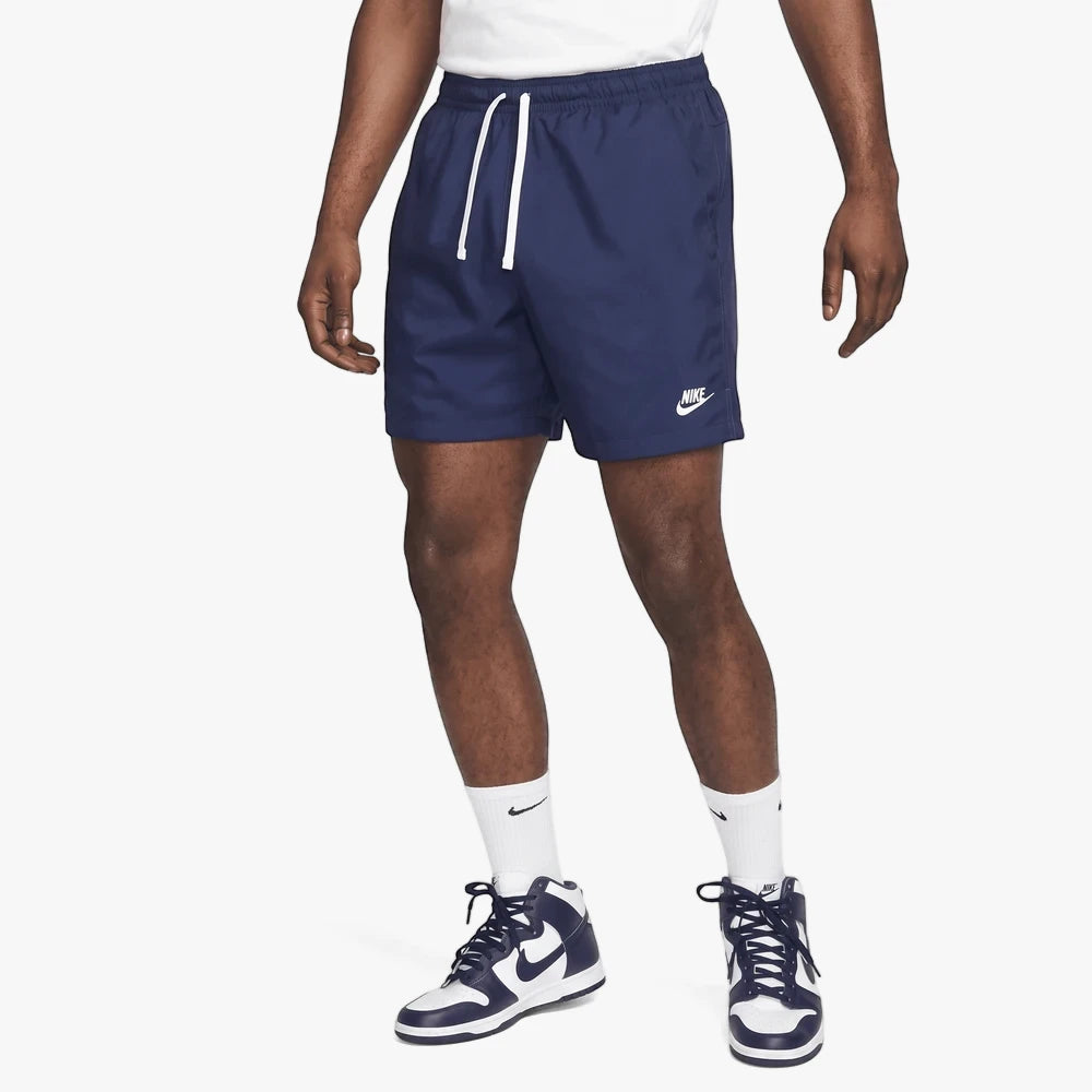 A male model wears navy blue Nike Spe Woven Flow shorts, featuring a white drawstring and Nike logo, paired with white socks