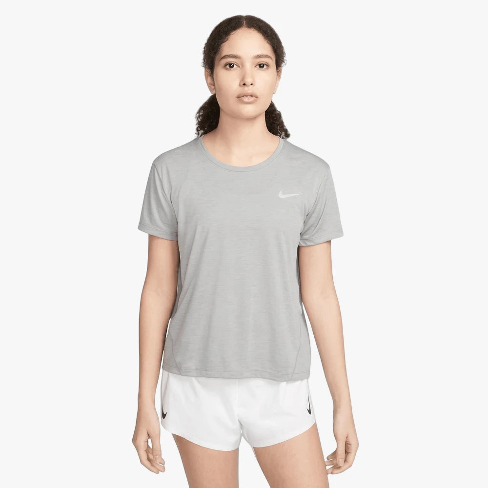 A woman models a grey Nike Miler Running Short Sleeve Tee and white shorts, standing confidently with a neutral expression.