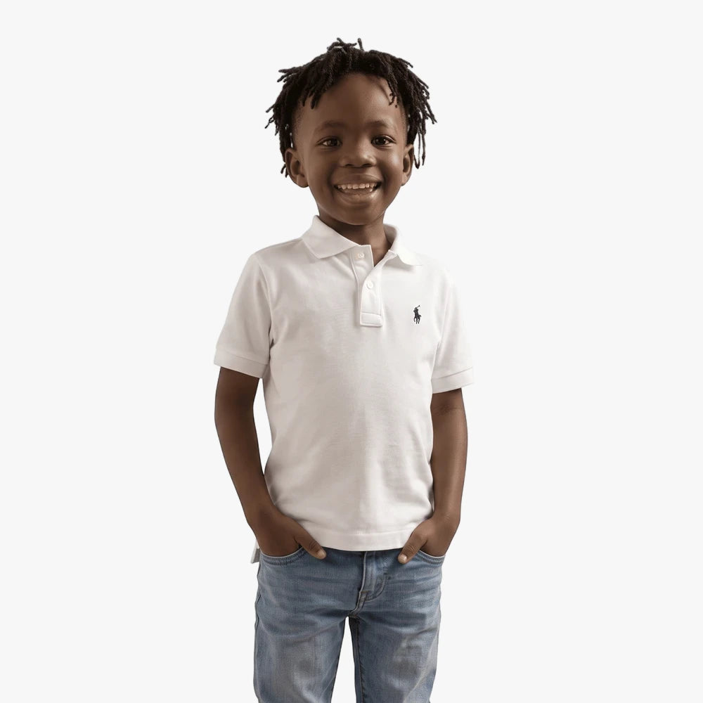 Smiling boy wearing a white short sleeve polo shirt and blue jeans in a studio setting.