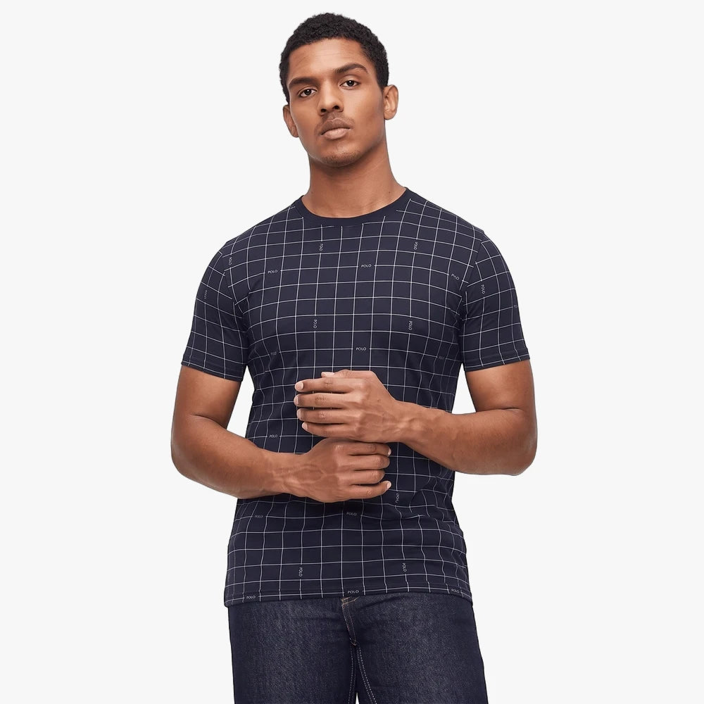 Male model in a navy Polo logo printed grid short sleeve tee and dark jeans, looking forward on a white background.