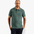 A male model wearing a dark green Pjc Overdyed short sleeve polo golfer shirt, with hands in pockets.