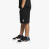 A boy wearing black Puma Essentials Jersey shorts, vibrant colorful sneakers, and blue socks, standing against a white