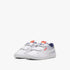 White Puma Kids Smash 3.0 sneakers with three velcro straps, blue stripes, and a red logo, shown from a low angle.