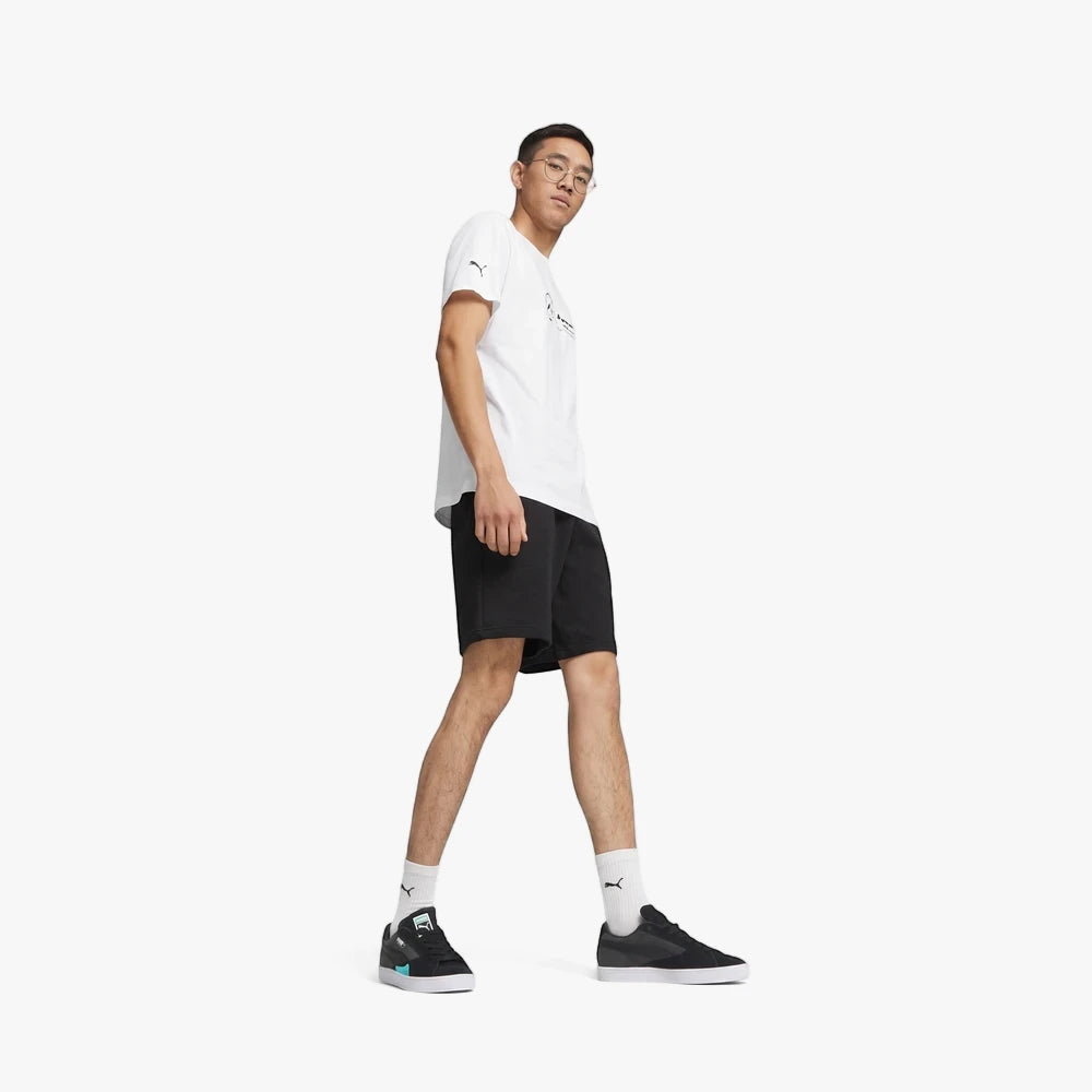 A male model wears a white Puma Mens Mapf1 Logo Short Sleeve Tee and black shorts, walking casually.
