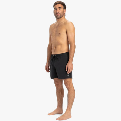 Man wearing black Quiksilver Everyday Solid Volley 15" shorts, standing full body on a white background. The shorts feature