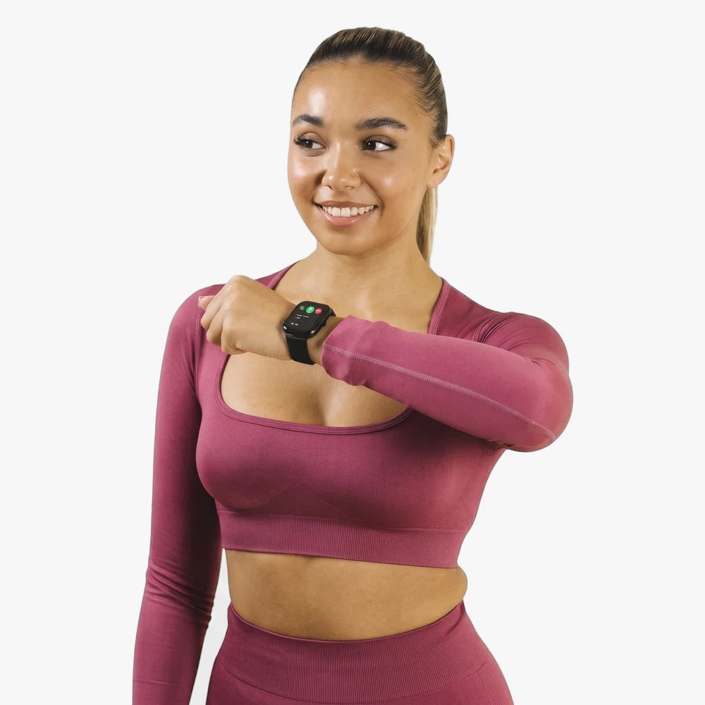 A smiling woman wearing a Reflex Active Series 23 black case and black silicone strap smartwatch on her left wrist.