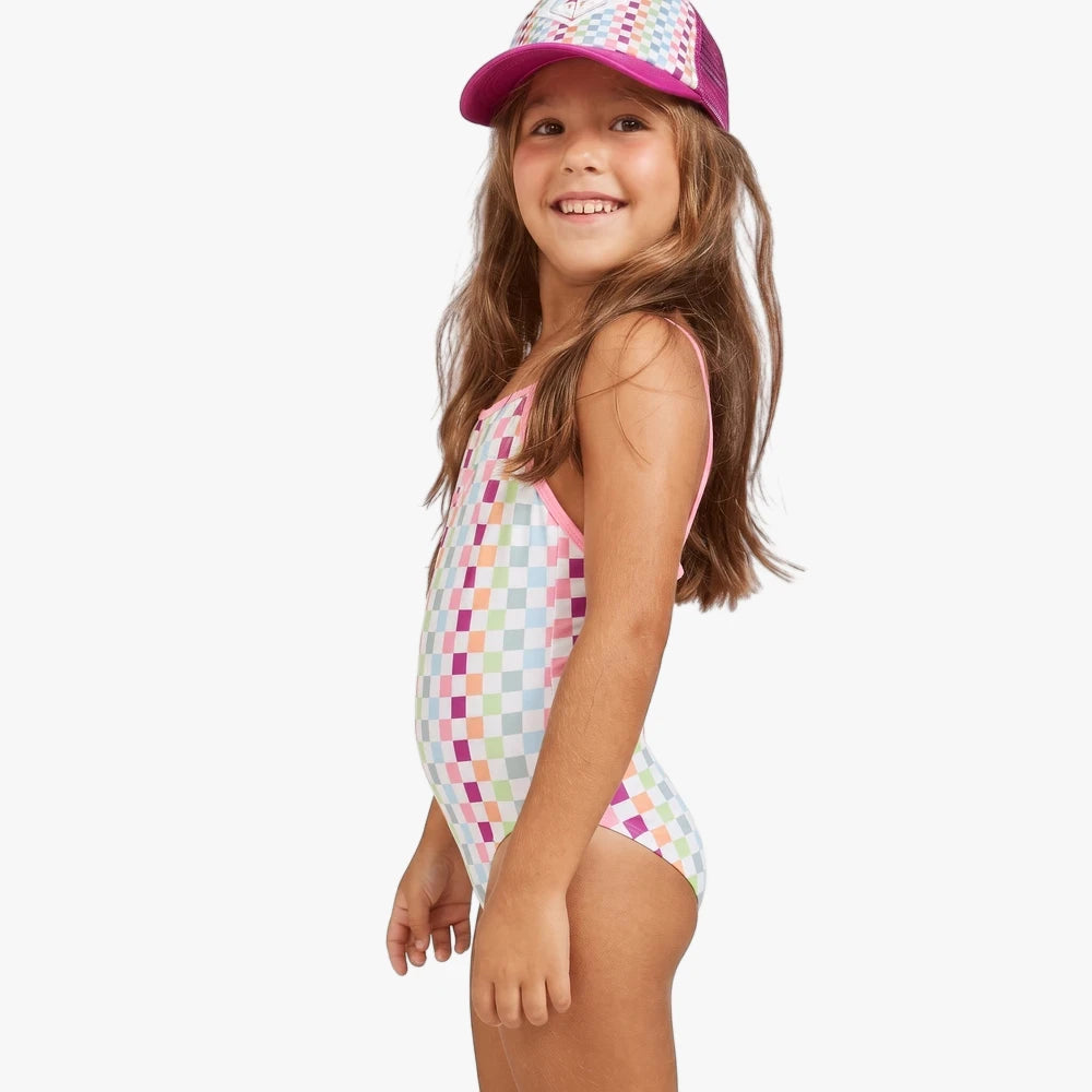 Young girl smiling, wearing a Roxy rainbow checkered one-piece swim suit with pink trim and a matching pink trucker cap,
