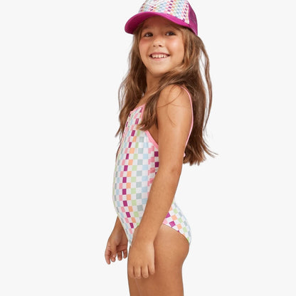 Young girl smiling, wearing a Roxy rainbow checkered one-piece swim suit with pink trim and a matching pink trucker cap,
