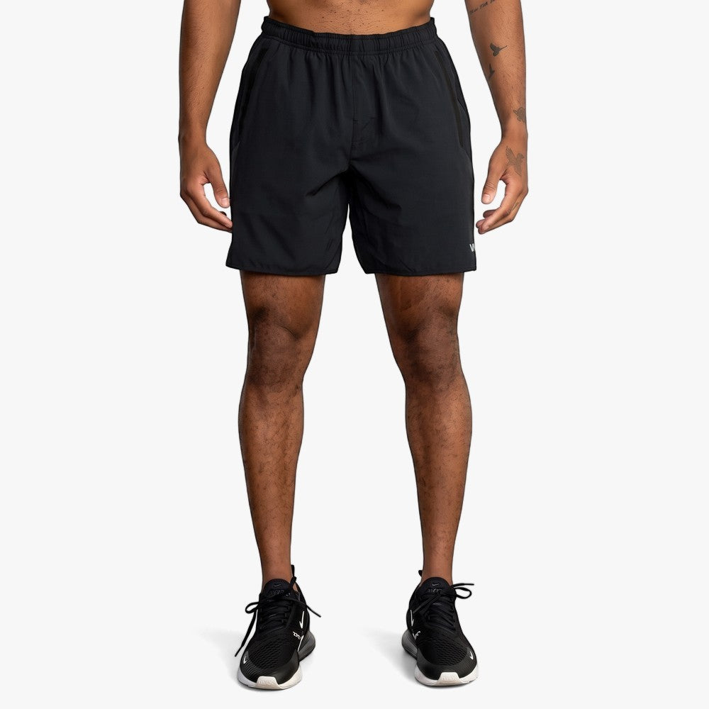 A full body image of a man wearing black Rvca Mens Yogger 17" Stretch Shorts and black sneakers, posing on a white