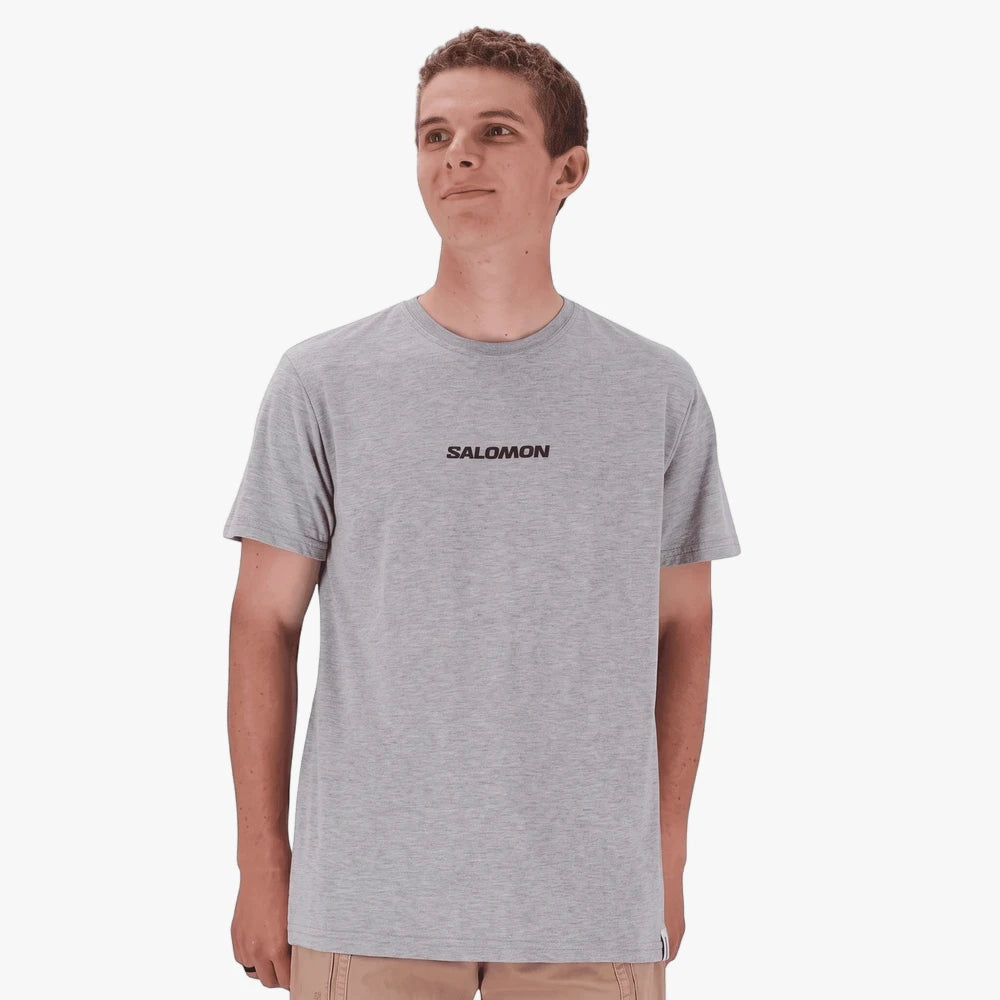 A male model wearing a grey Salomon logo short sleeve t-shirt, standing and looking to the right.