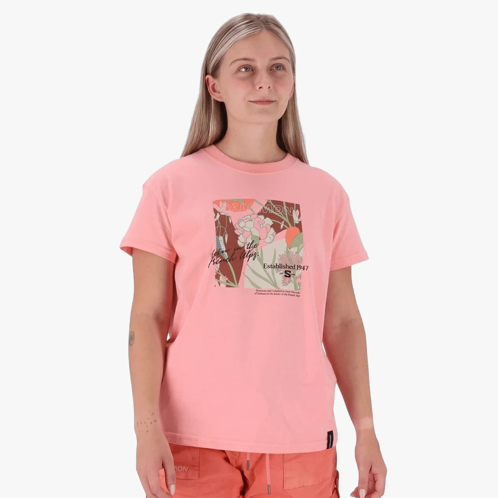 Woman wearing a Salomon Freedom Short Sleeve Tee in Murex Shell pink, featuring a unique floral graphic print.