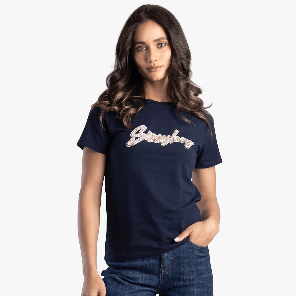 A woman models a navy Sissy Boy regular sequin and pearl short sleeve tee with blue jeans, posing with hand in pocket.