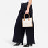 Sissy Boy Willow Bag mini tote handbag in stone canvas with tan handles, carried by a model wearing dark pants and boots.
