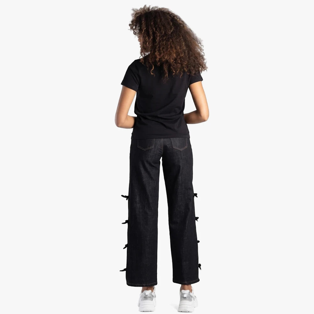 Back view of a woman wearing a black Sissy Boy regular fit short sleeve tee and dark wash wide-leg jeans with bow details.