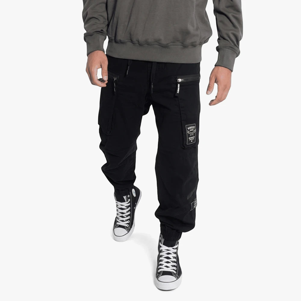 Close-up of a man wearing black Soviet elasticated cargo pants with zippered pockets and black high-top sneakers.