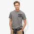 Male model wearing a grey Superdry Vintage Athletic Chest Tee, with a plaid shirt tied around his waist and khaki pants,