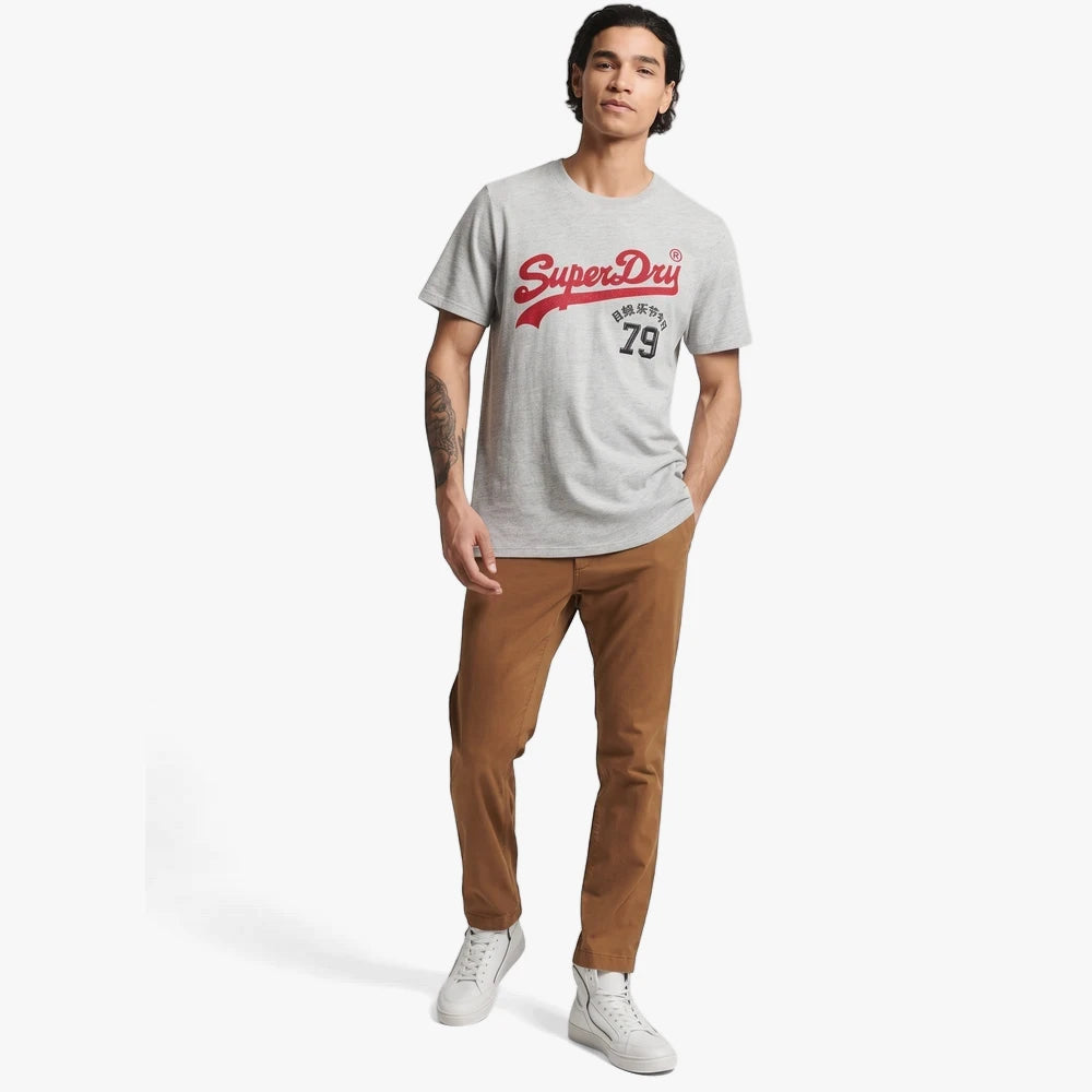 Male model wearing a Superdry Mens Vintage Vl Interest Short Sleeve Tee in Athletic Grey Marl with red logo, brown pants,