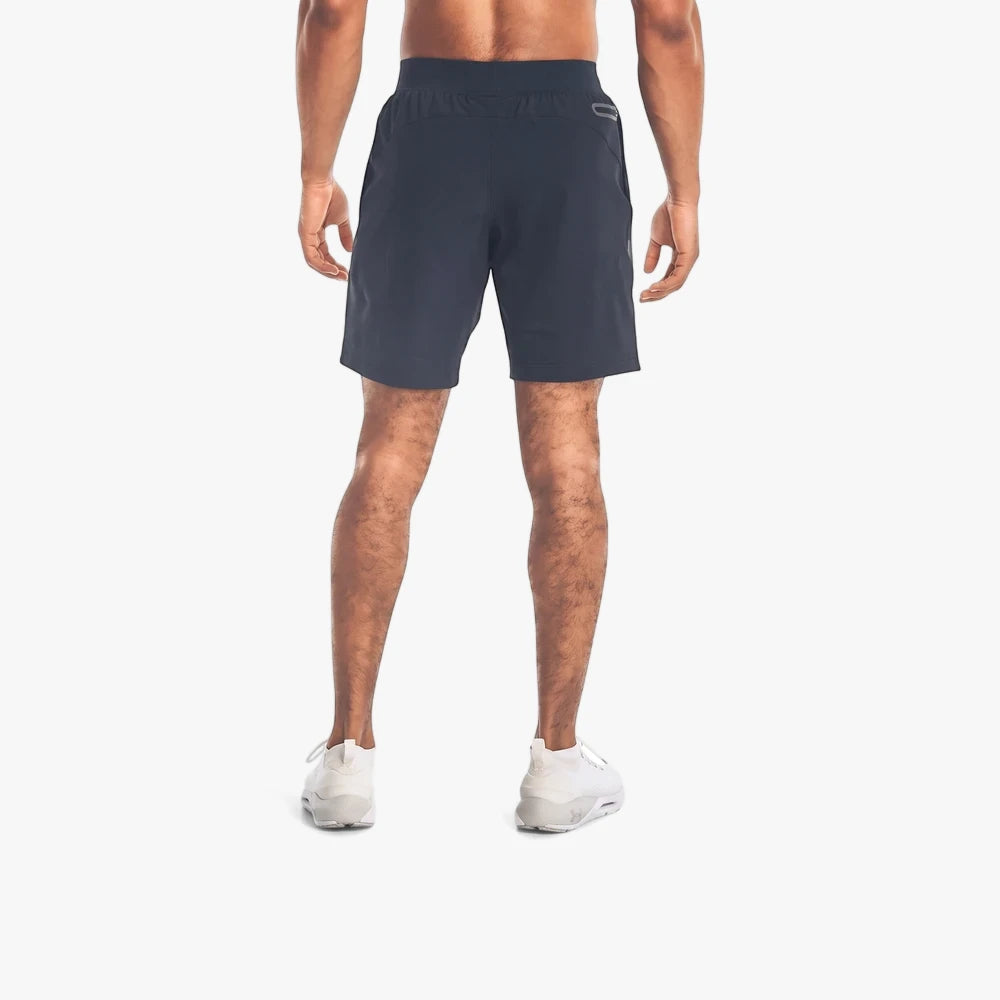 A man from the back wears black Under Armour Unstoppable Shorts and white sneakers, standing against a white background.